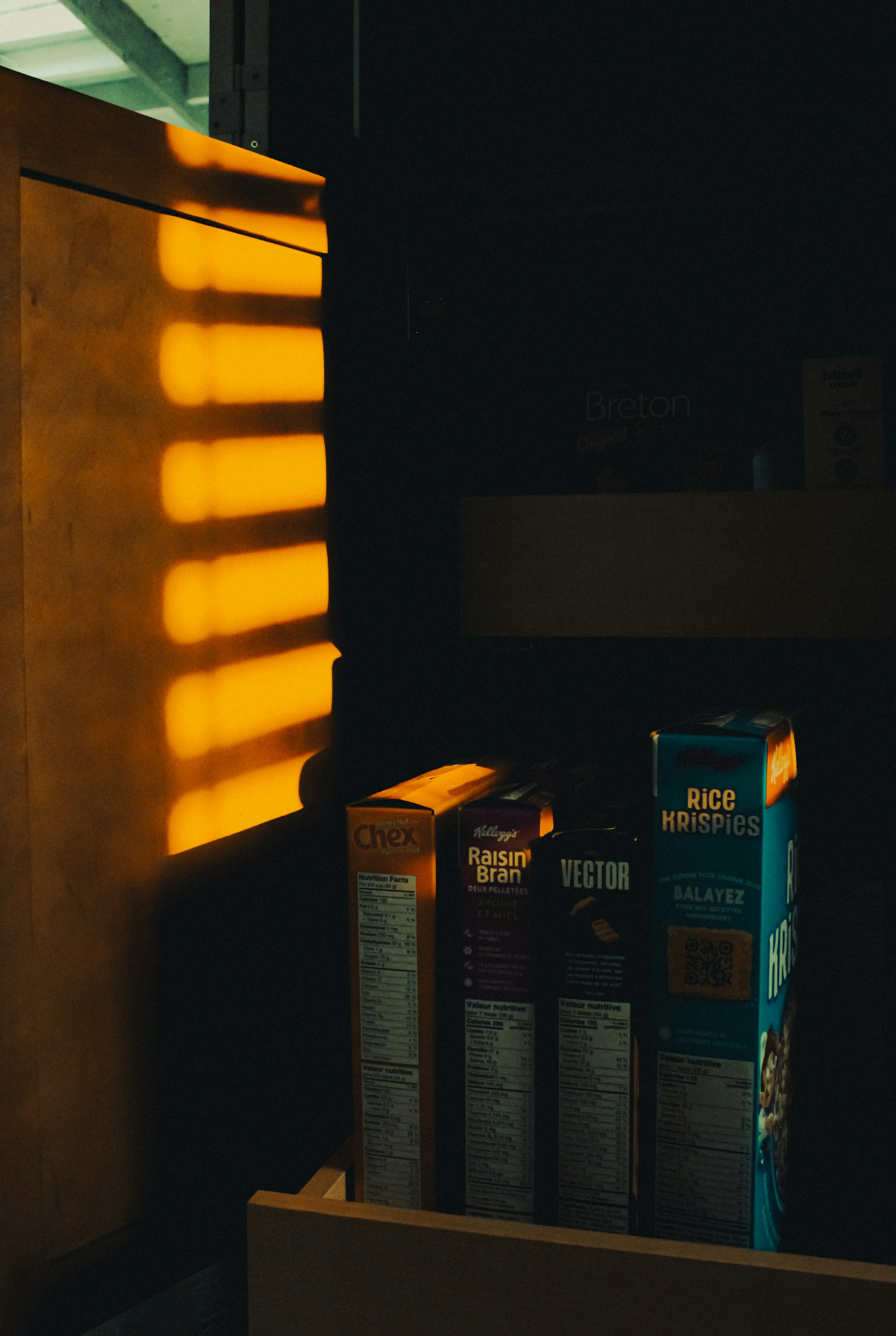 Cereal boxes lined up on a warehouse shelf in dramatic low light — SKU records with attributes to be inspected, backfilled, and augmented