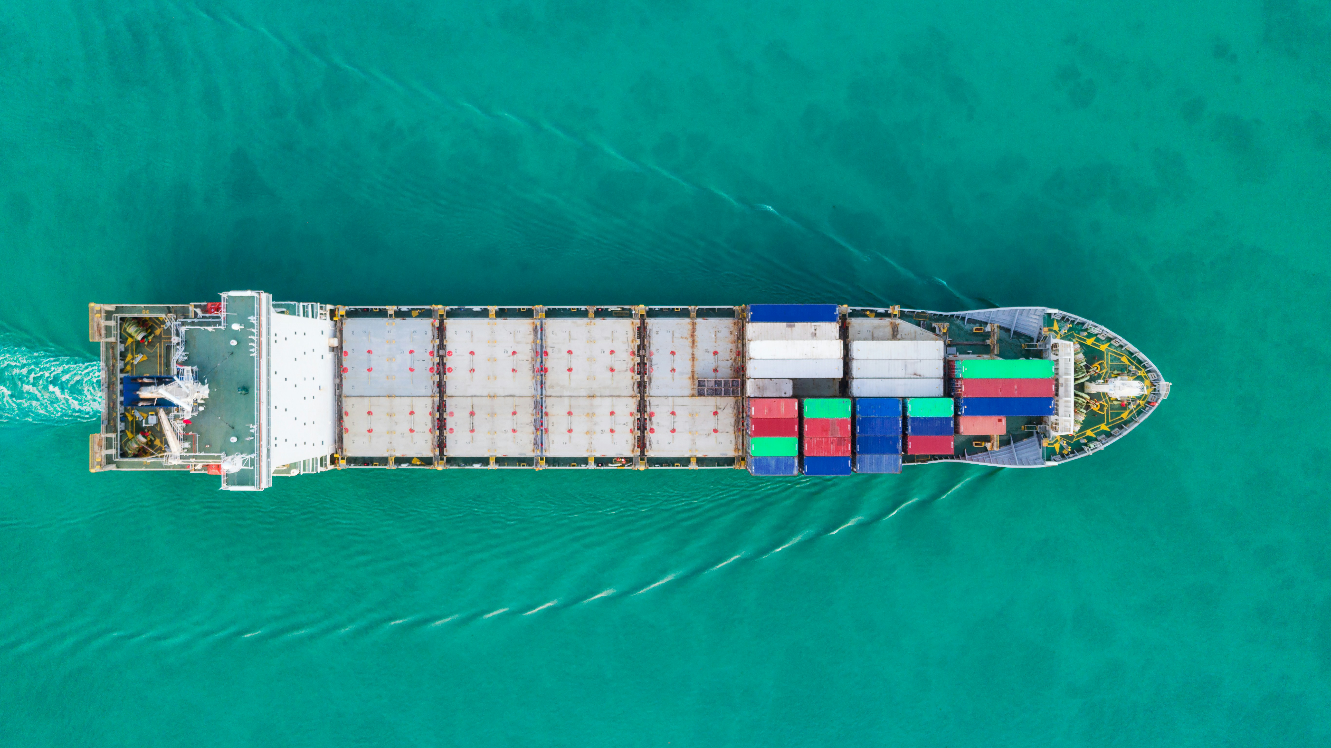 Cargo ship aerial from above on bright turquoise water, mix of containers and bulk cargo
