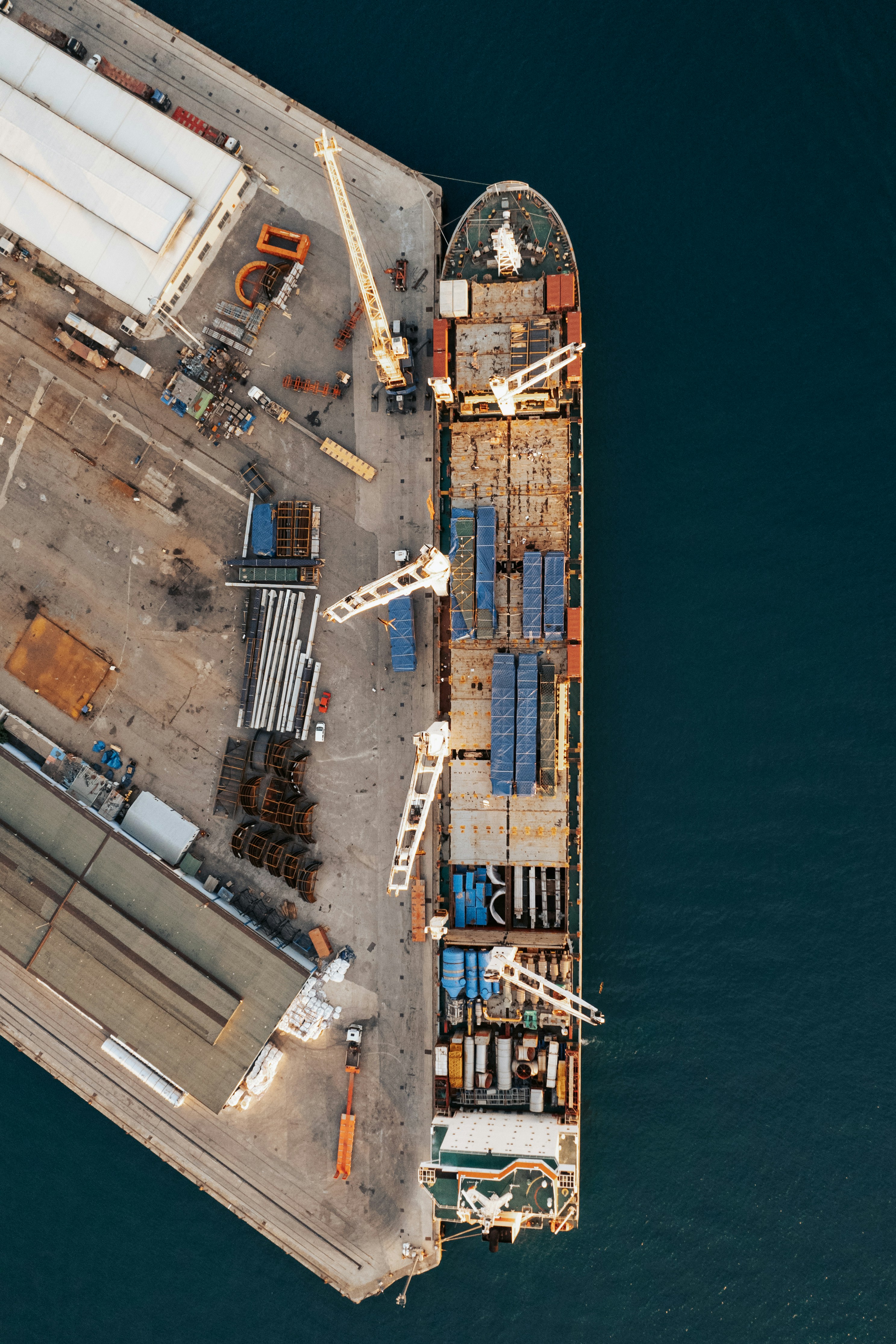 Aerial view of a cargo ship docked beside port cranes