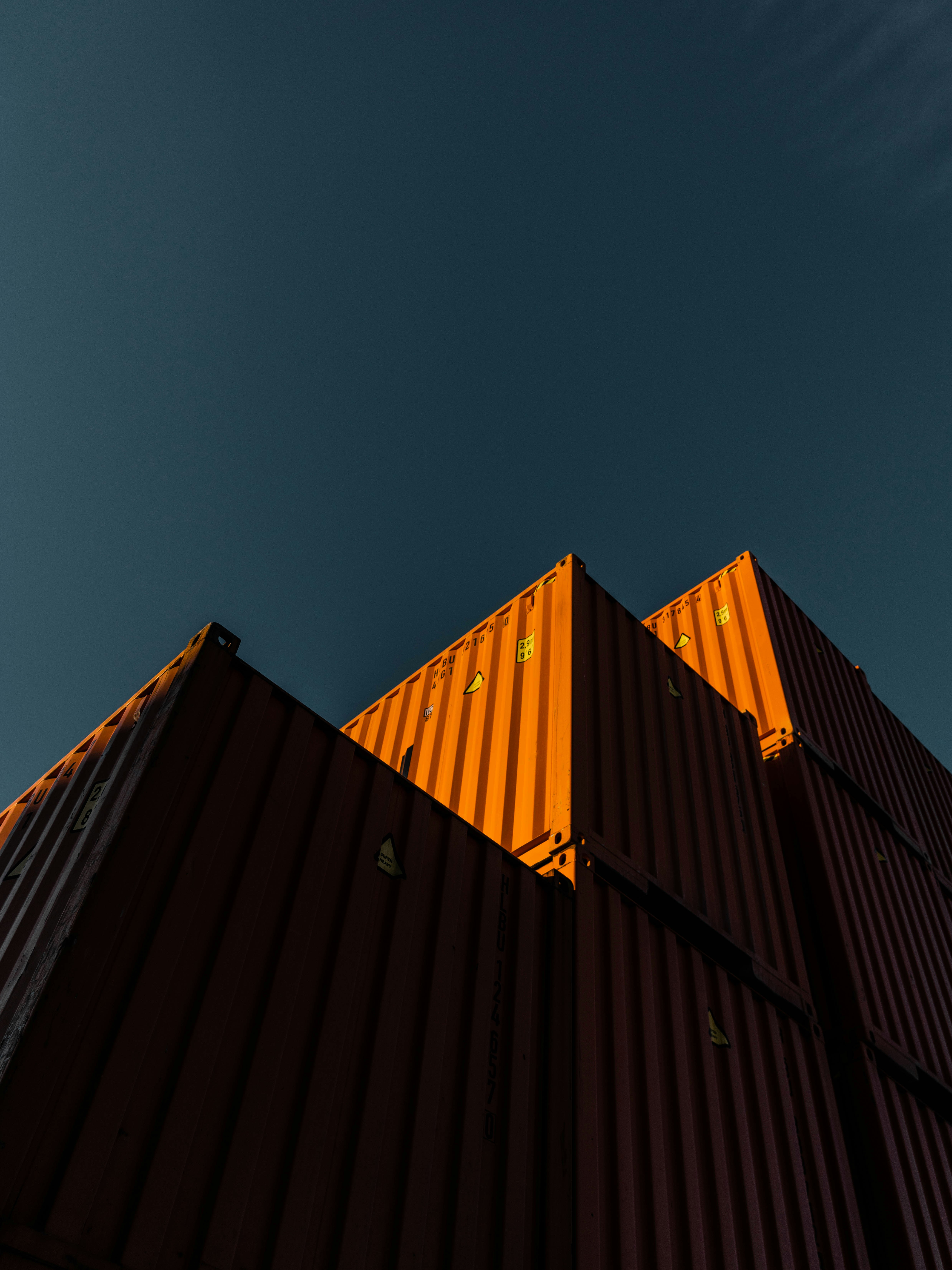 Stacked shipping containers shot from below against dark sky, dramatic orange sunset light on upper containers