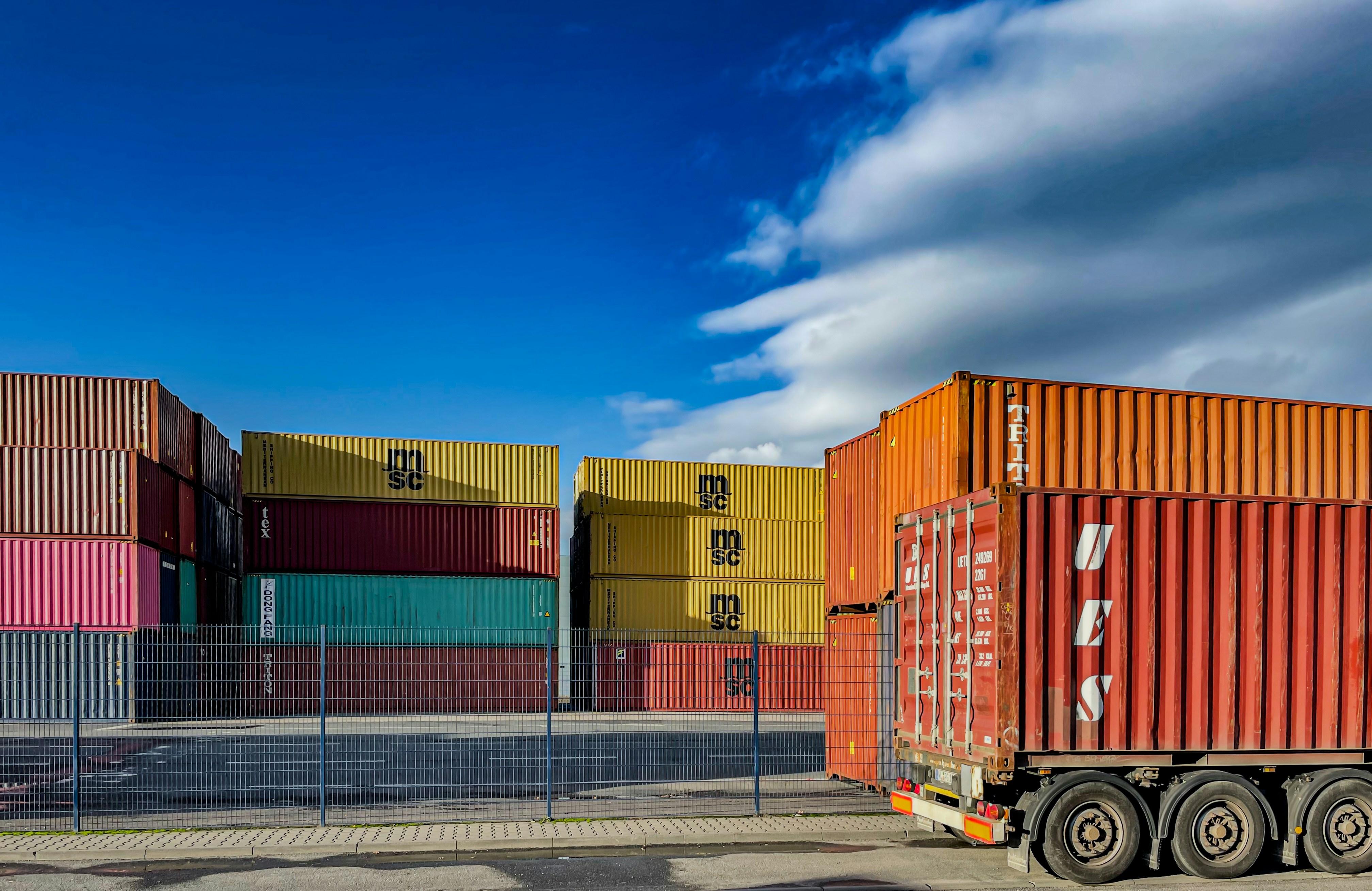 Stacked colourful shipping containers at yard with truck trailer, bright blue sky