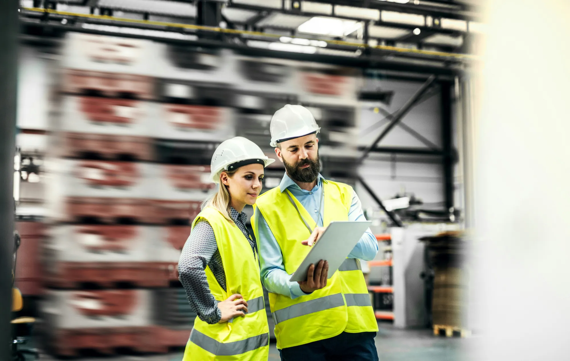Warehouse professionals in safety vests reviewing operational data together on a tablet