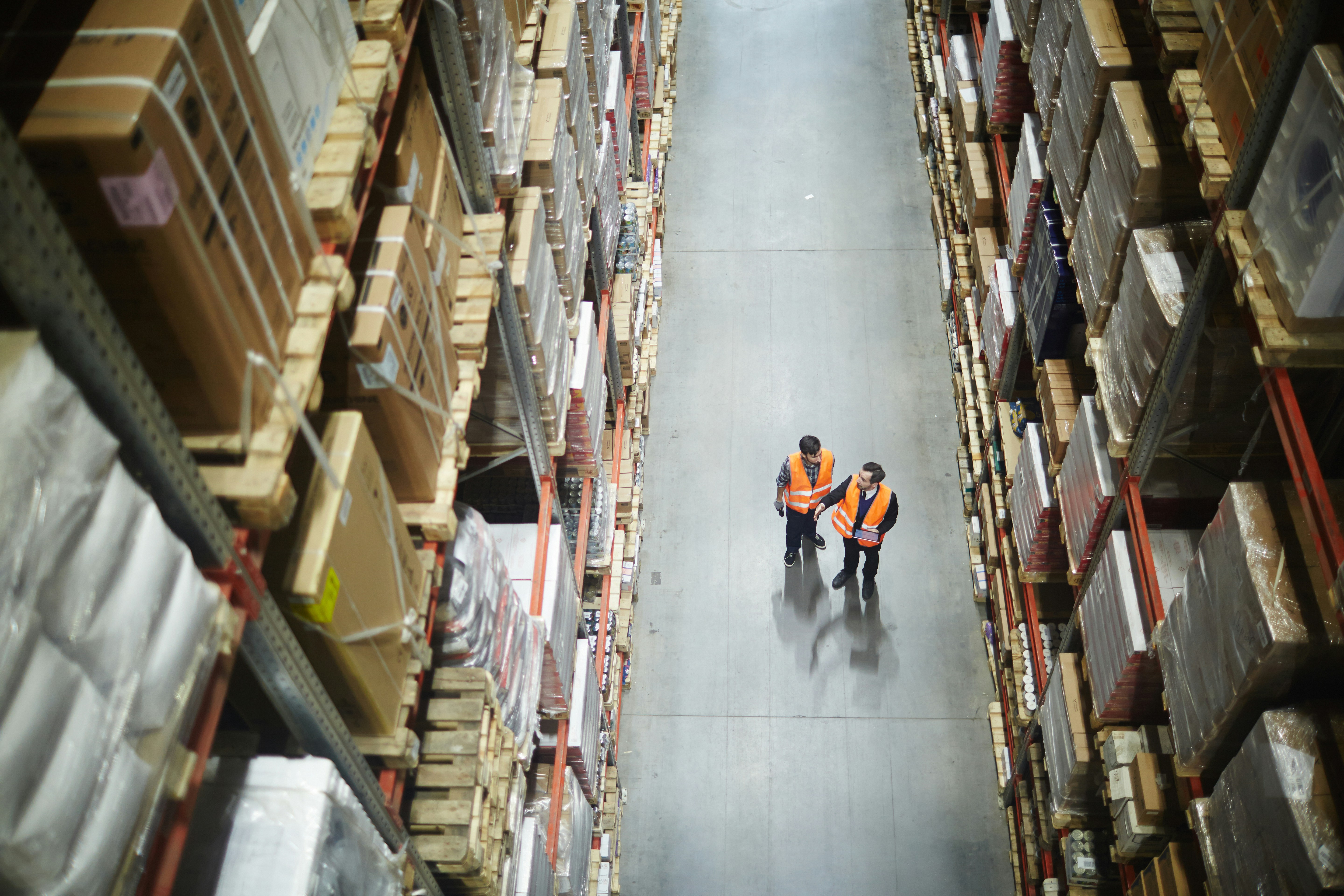 Overhead view of two warehouse workers reviewing a document in a long aisle