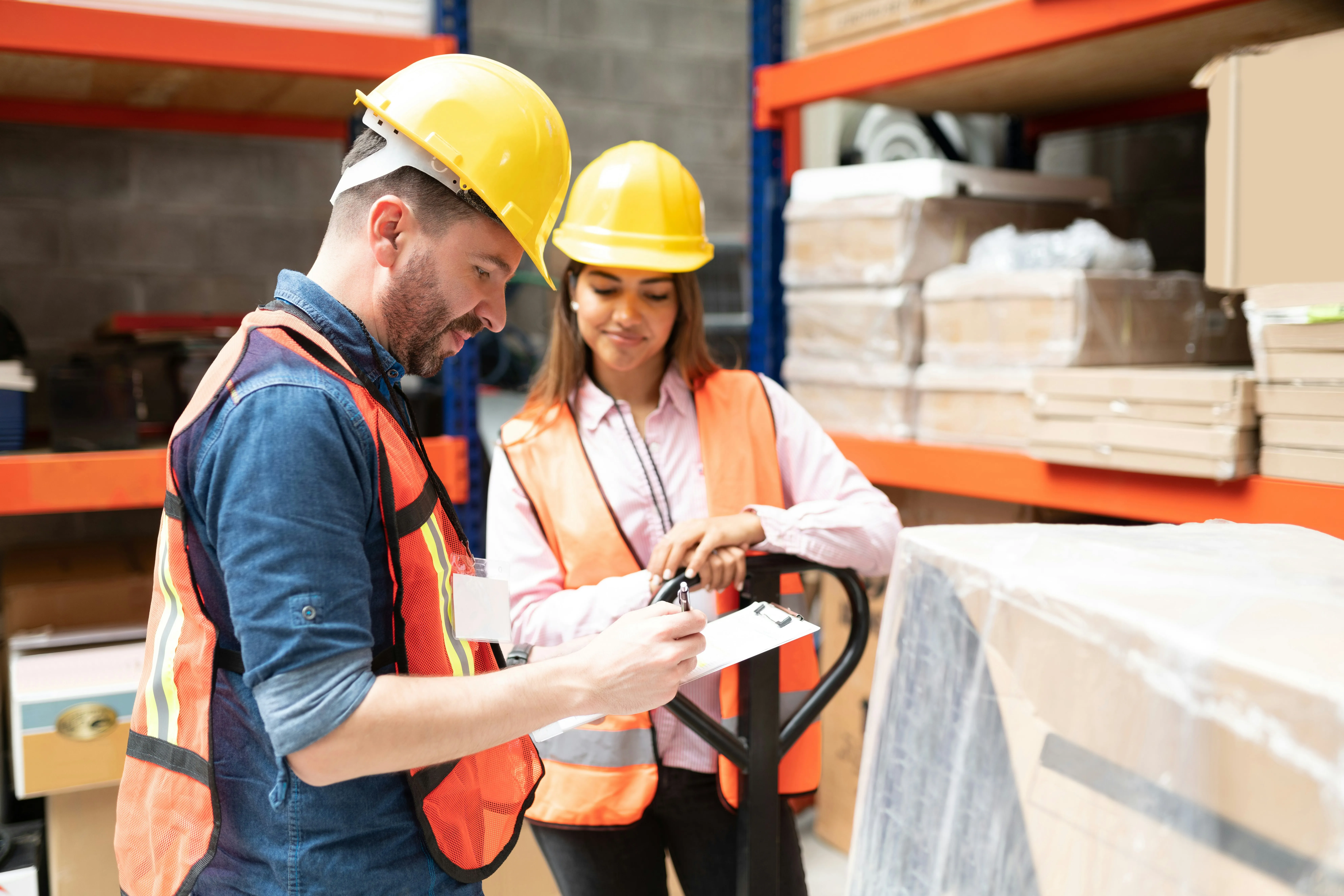 Warehouse workers reviewing a clipboard beside a pallet jack